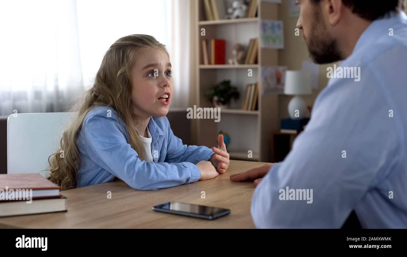 Père discutant de la dépendance des gadgets avec sa petite fille, conflit de génération Banque D'Images
