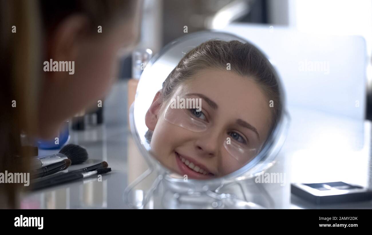 Femme avec des taches de gel sous les yeux regardant dans le miroir et sourire, soins anti-âge Banque D'Images