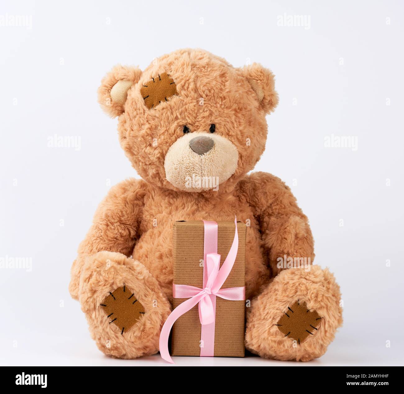Grand ours en peluche beige avec des taches organiser cadeau en carton enveloppé dans du papier brun, attaché avec du ruban de soie rose sur fond blanc, joyeux anniversaire et valen Banque D'Images