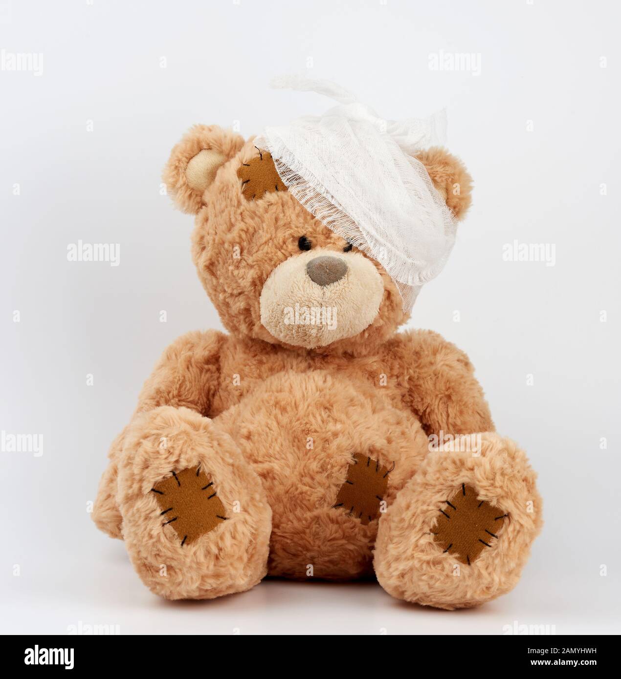 Grand ours en peluche avec une tête bandée dans un bandage médical blanc sur fond blanc, concept du traumatisme des enfants, jouet avec des correctifs Banque D'Images