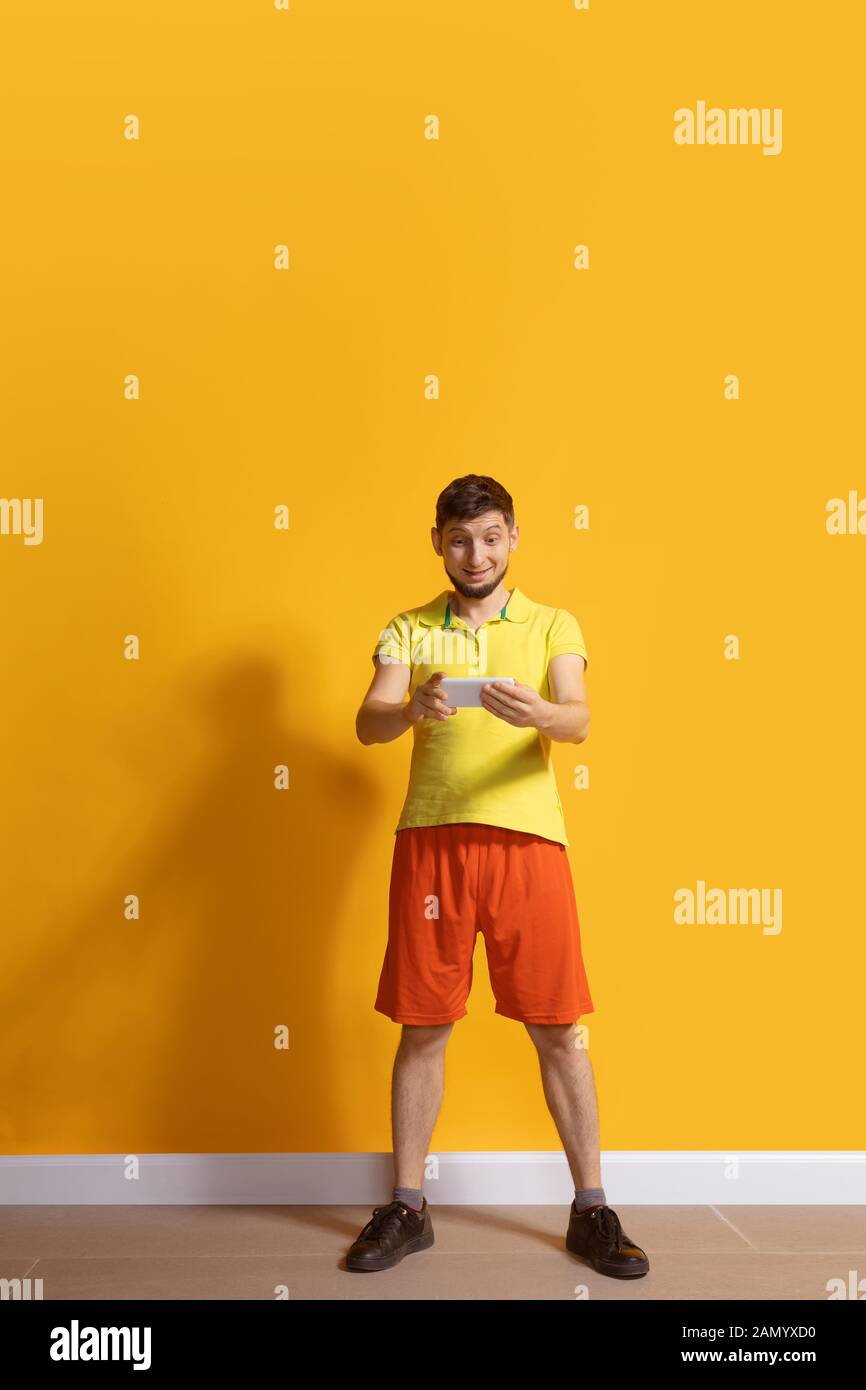 Joyeux sourire. Jeune homme caucasien utilisant smartphone, serfing, chat, Paris. Portrait complet isolé sur fond jaune. Concept des technologies modernes, des millénaires, des médias sociaux. Banque D'Images