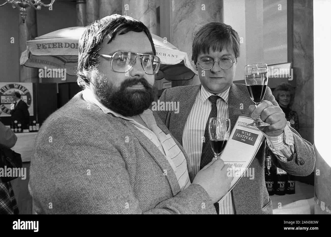 1988, historiques, deux hommes tenant des verres de vin rouge à l'intérieur d'un hall à un festival du vin, England, UK. Banque D'Images