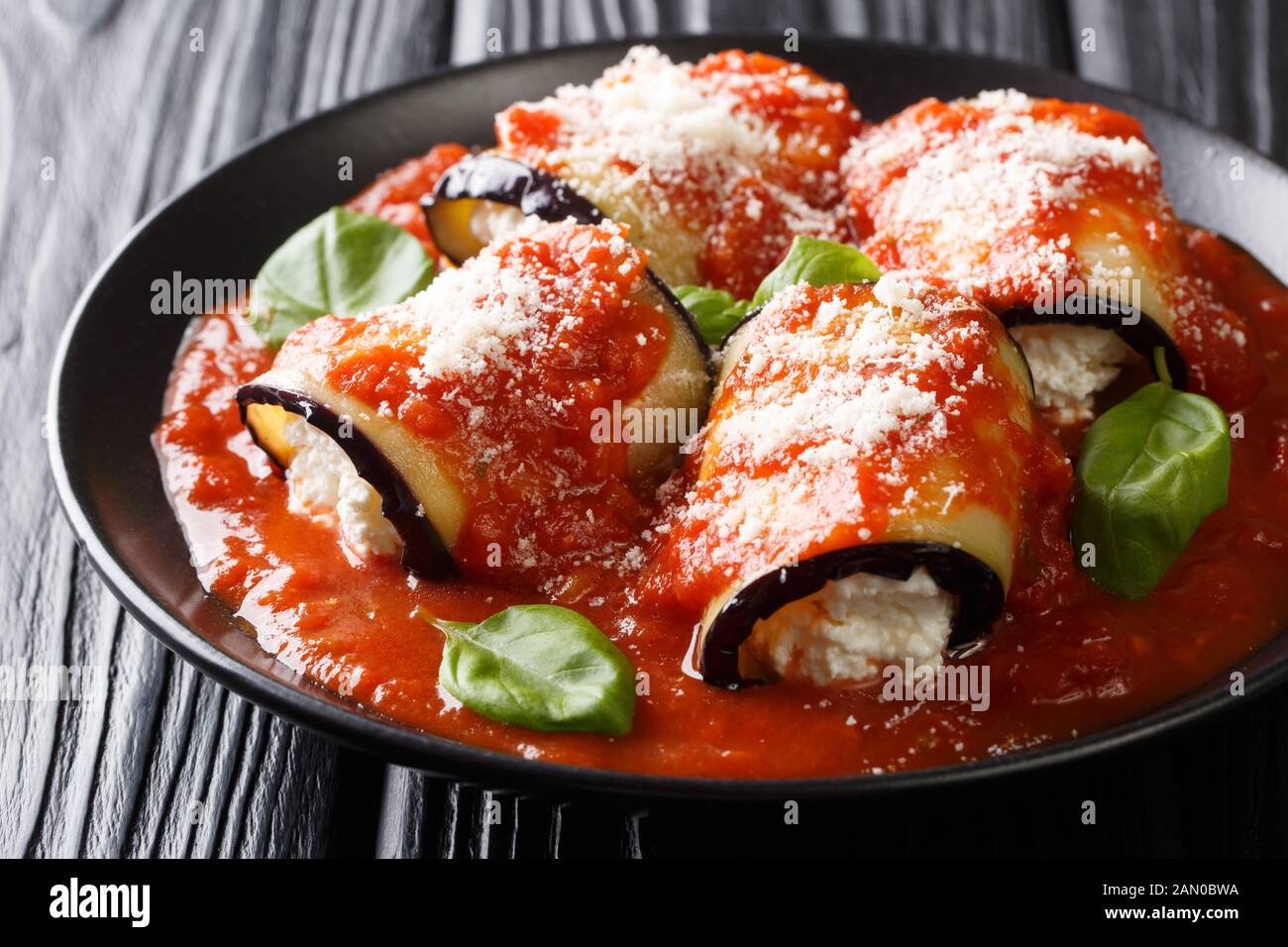 Petits pains d'aubergine cuits à la ricotta dans la sauce tomate et servis avec le parmesan et le basilic dans une assiette sur la table. Horizontale Banque D'Images