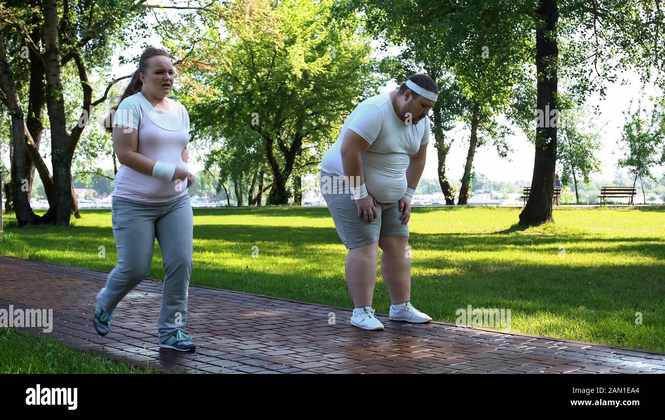 Joyeux chubby fille à l'extérieur de l'homme obèse fatigué après le jogging, épuisant les entraînements Banque D'Images