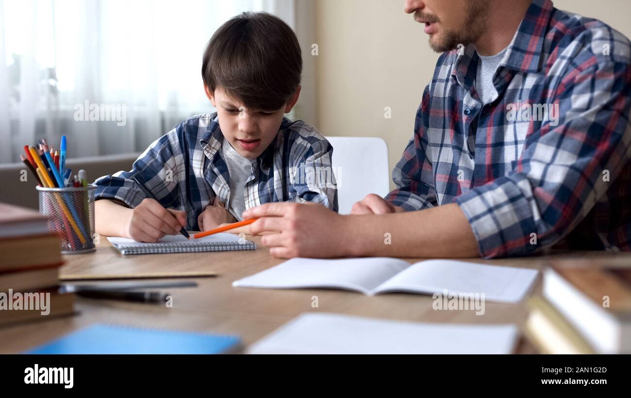 Papa assis à la table et faire son fils capricieux pour faire des devoirs, l'éducation Banque D'Images