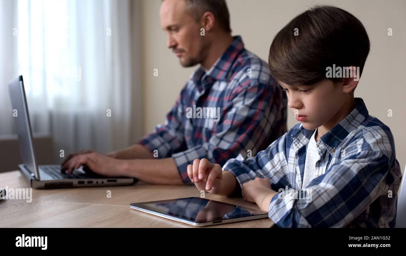 Enfants défilant sur tablette, père travaillant sur ordinateur portable, manque d'attention Banque D'Images