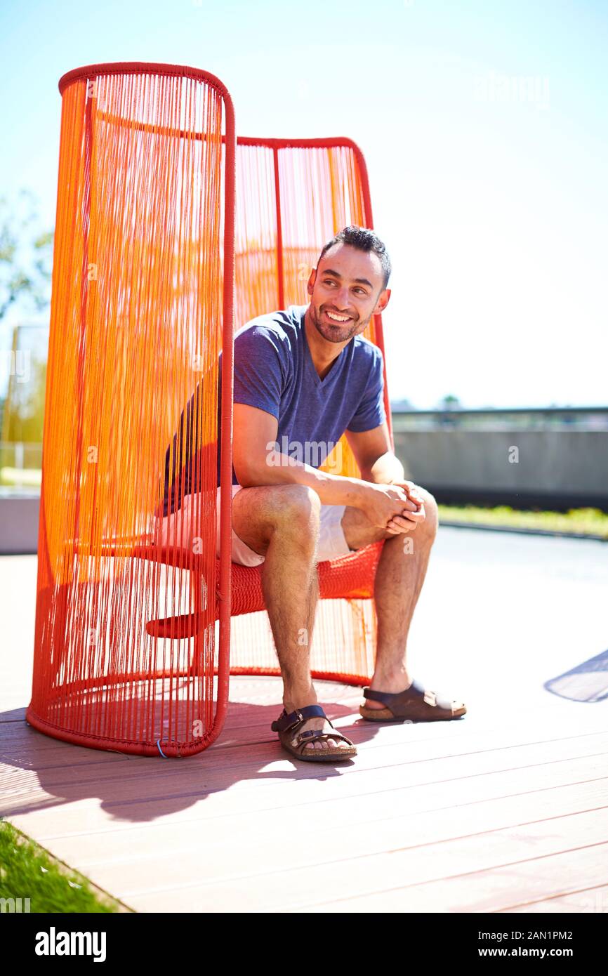 Un homme assis dehors dans une chaise moderne colorée. Banque D'Images