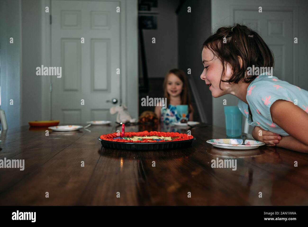 portrait de jeune fille soufflant de bougie d'anniversaire à une table Banque D'Images