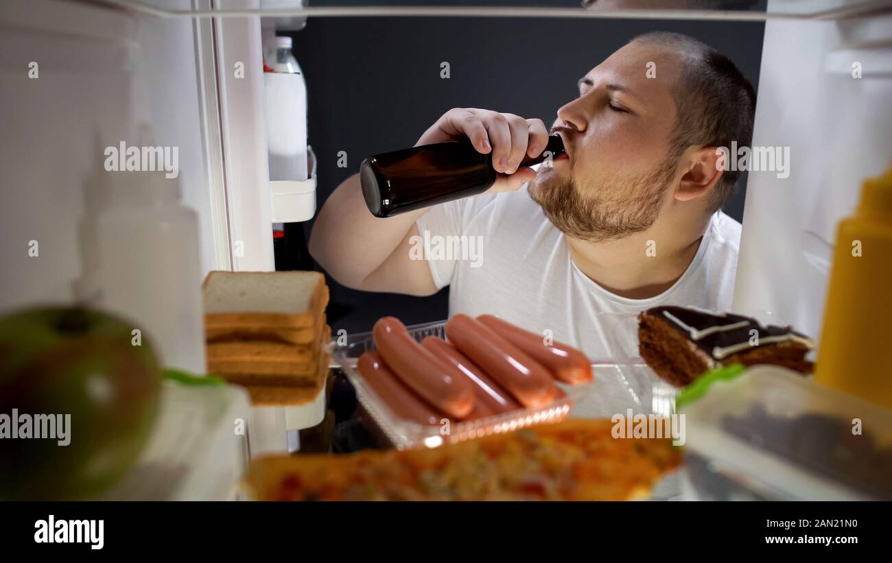 Fat Man drinking beer avec plaisir du frigo la nuit, mode de vie malsain Banque D'Images