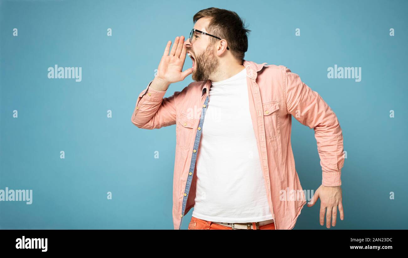 Caucasian man crier très fort sur le côté, faire une annonce importante, tenant la main près de la bouche, avec l'exemplaire de l'espace. Banque D'Images