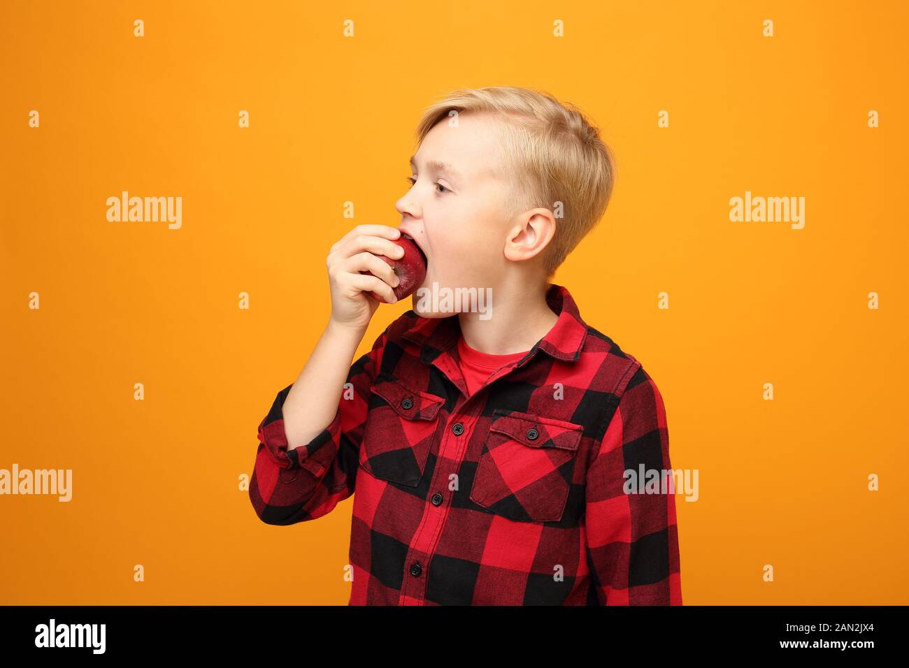 Le garçon mange des fruits, une alimentation saine pour les enfants. Beau garçon caucasien souriant dans la chemise rouge sur fond jaune. Horizontale, droite. Banque D'Images