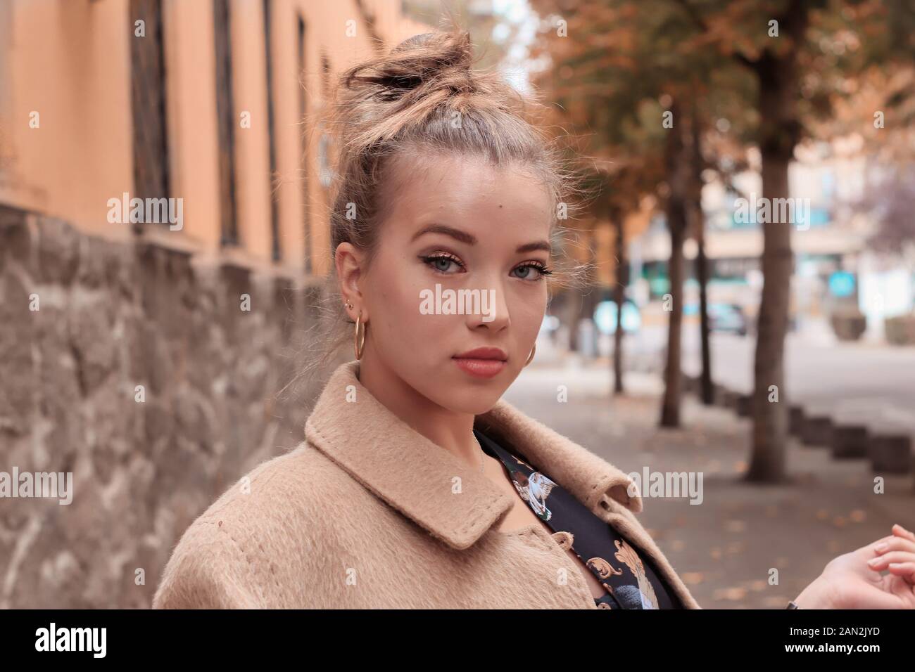 Belle blonde jeune femme avec manteau beige et cheveux recueillis Banque D'Images