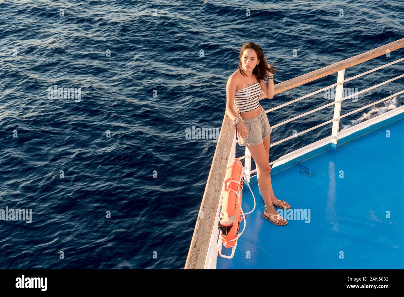 Dans l'adolescence asiatiques tube top et short debout sur le pont bleu à côté de l'orange life preserver sur ferry allant à Lesbos Banque D'Images