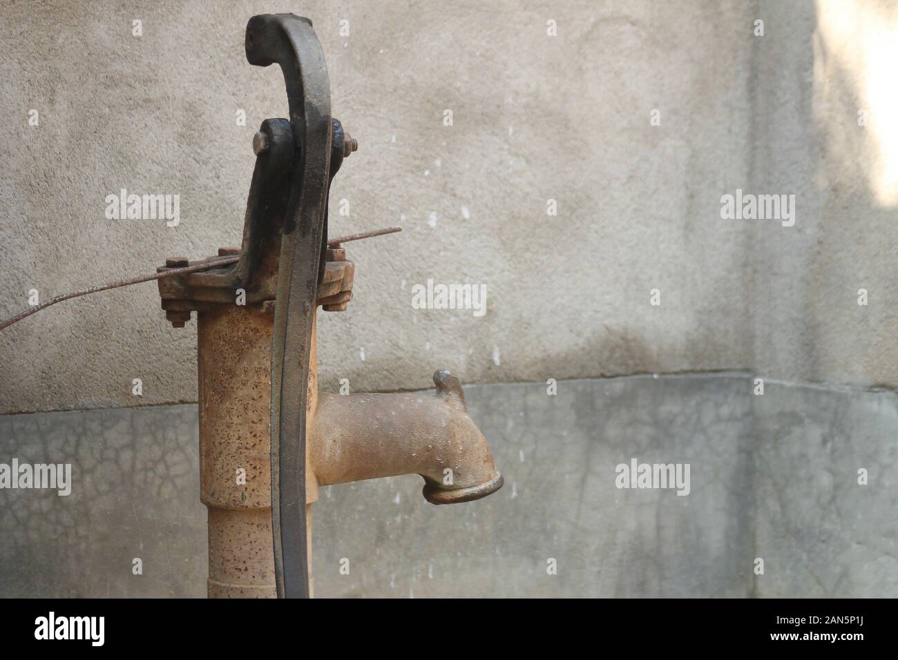 Vieille pompe à eau à main rouillée contre le mur de ciment fissuré dans un cadre extérieur rural Banque D'Images