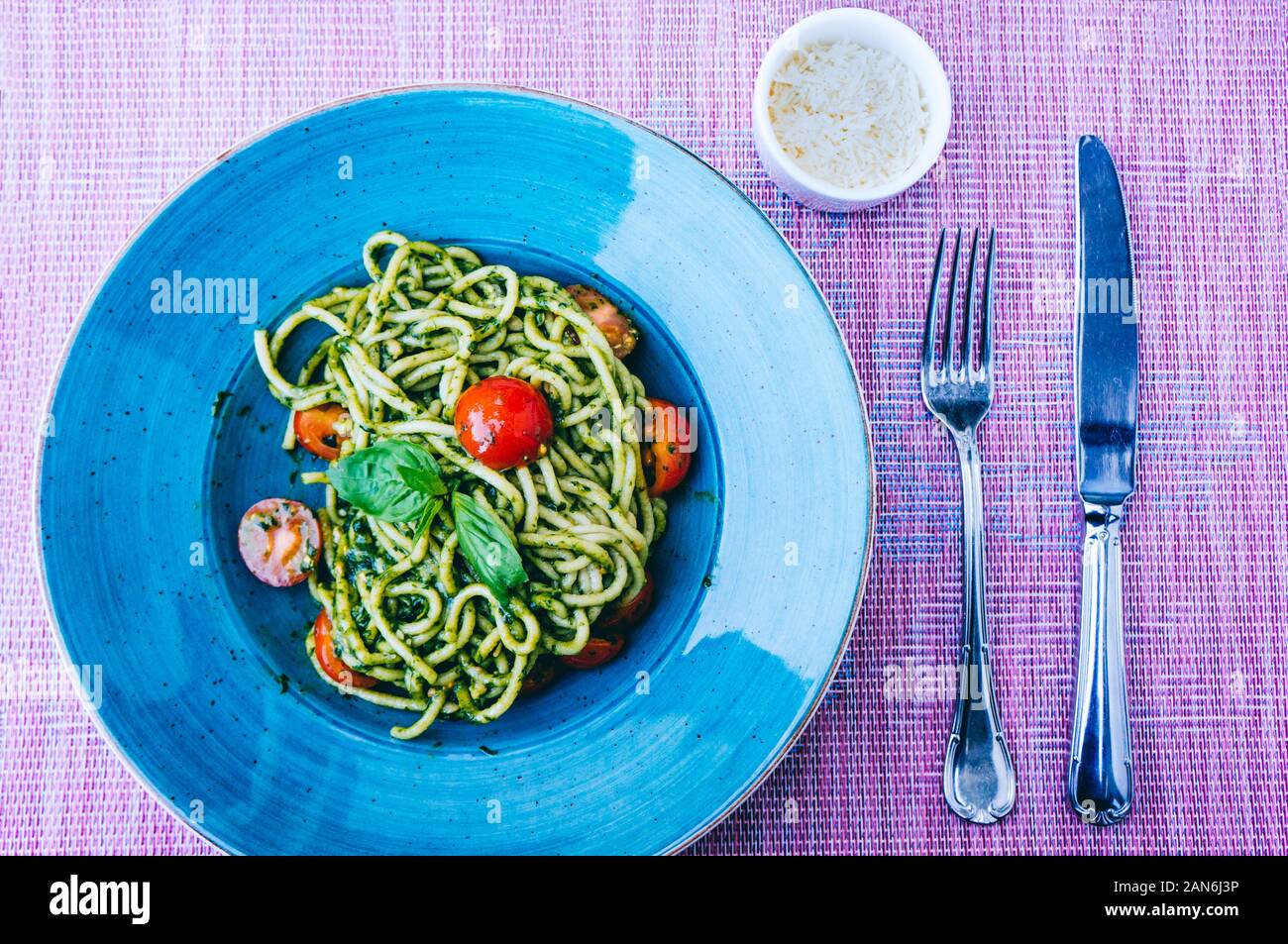 Maison Italienne pici pâtes avec sauce pesto vert et tomates cerises sur plaque bleue avec du parmesan et de couverts Banque D'Images