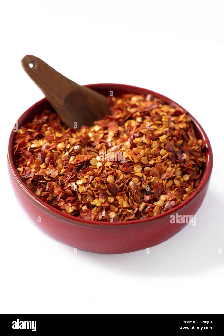 Close up of hot chili flakes dans un bol de couleur rouge avec cuillère isolé sur fond blanc Banque D'Images