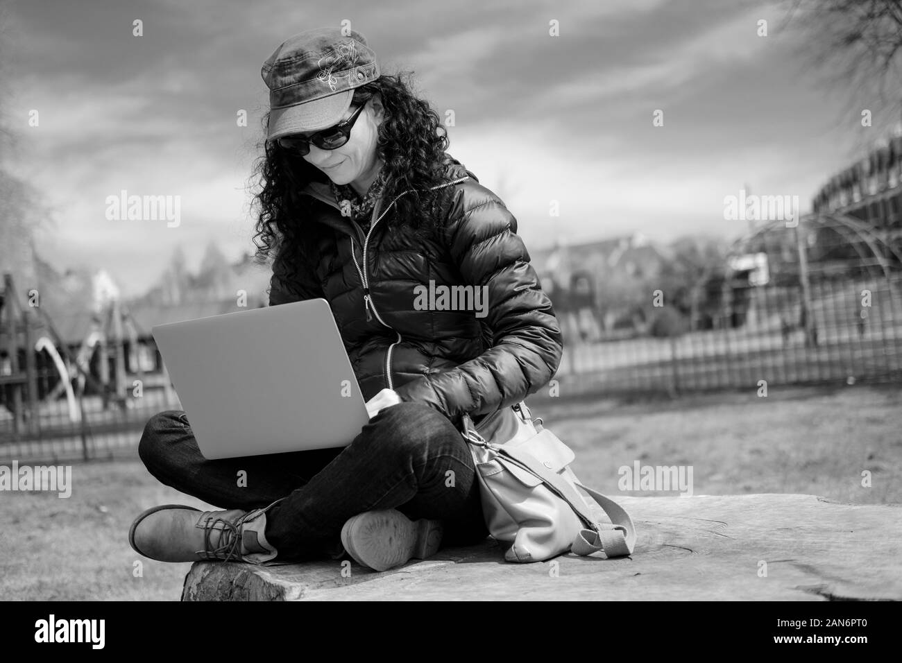 Portrait of middle-aged woman assis sur un tronc arbre dans un parc à l'aide d'un ordinateur portable en noir sur blanc Banque D'Images