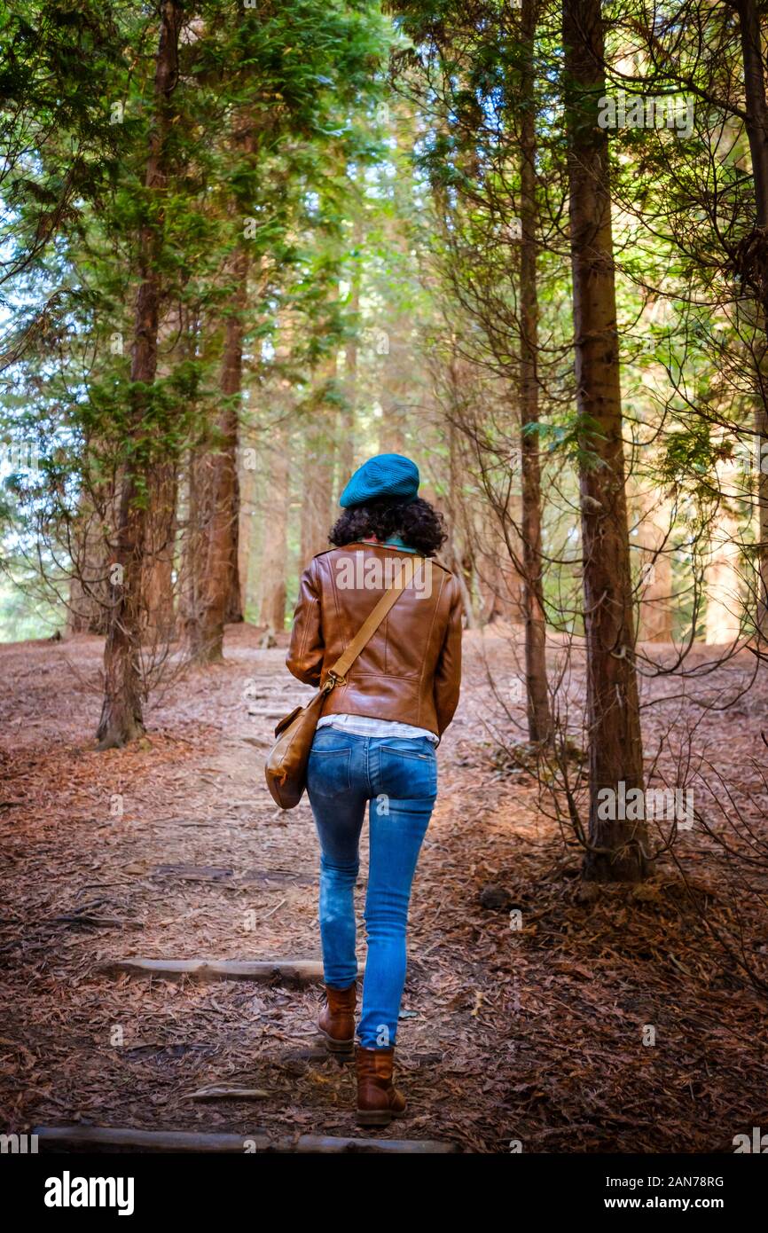 Femme portant un blouson de cuir brun et béret vert marche à travers une forêt Banque D'Images