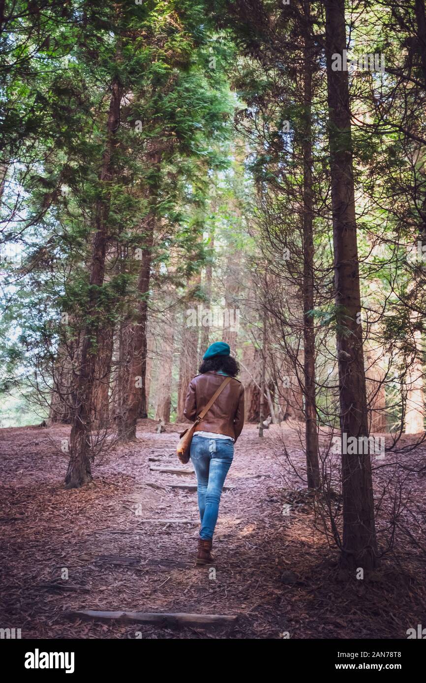 Femme portant un blouson de cuir brun et béret vert marche à travers une forêt Banque D'Images