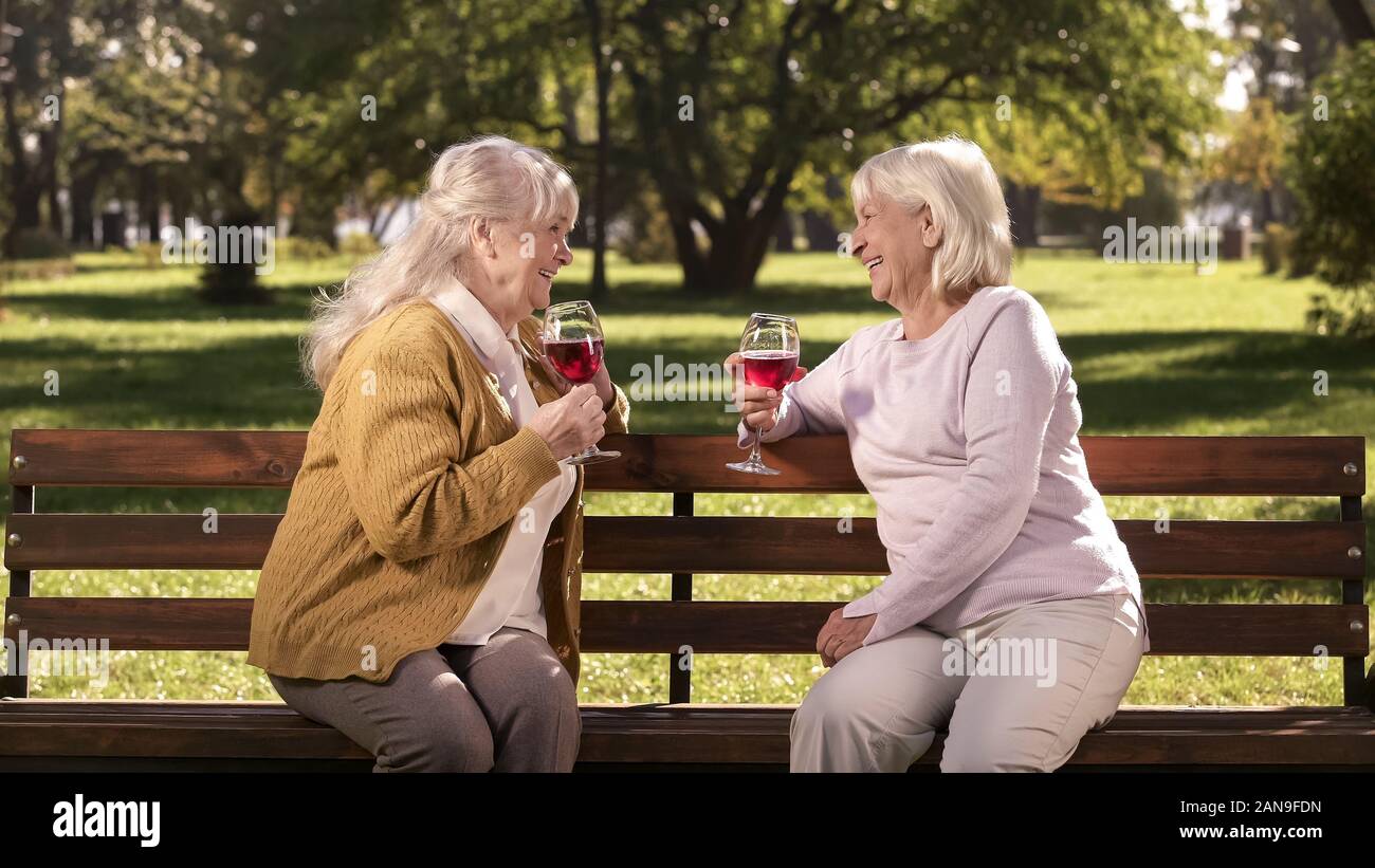 Deux femmes âgées bénéficiant du vin et à discuter sur un banc de parc en toute sécurité avec une assurance d'or Banque D'Images