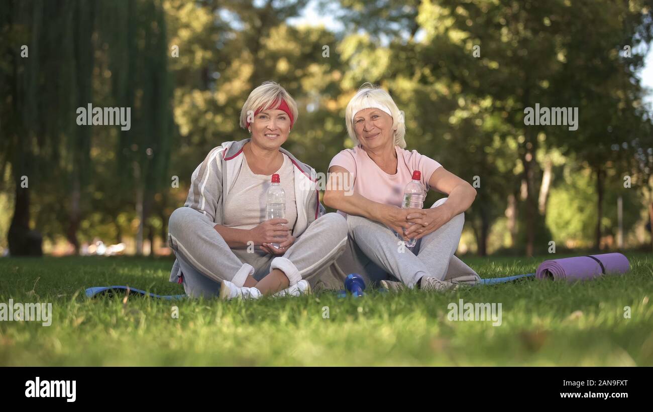 Deux femmes assises sur l'herbe, et l'appareil photo en souriant après avoir terminé le yoga Banque D'Images