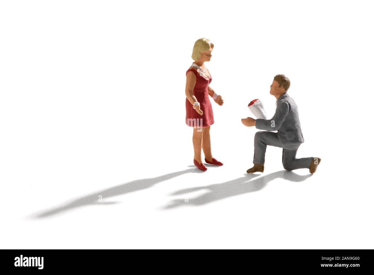 Scène Miniature de proposition d'engagement, avec un petit homme en costume gris, le bas sur son genou avec un bouquet de fleurs, qui se propose d'une femme en robe rouge. Banque D'Images