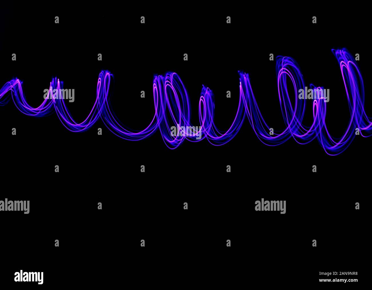 Une longue exposition light painting, vibrant rose et violet couleur en tourbillons abstraits contre un fond noir. La lumière peinture photographie. Banque D'Images