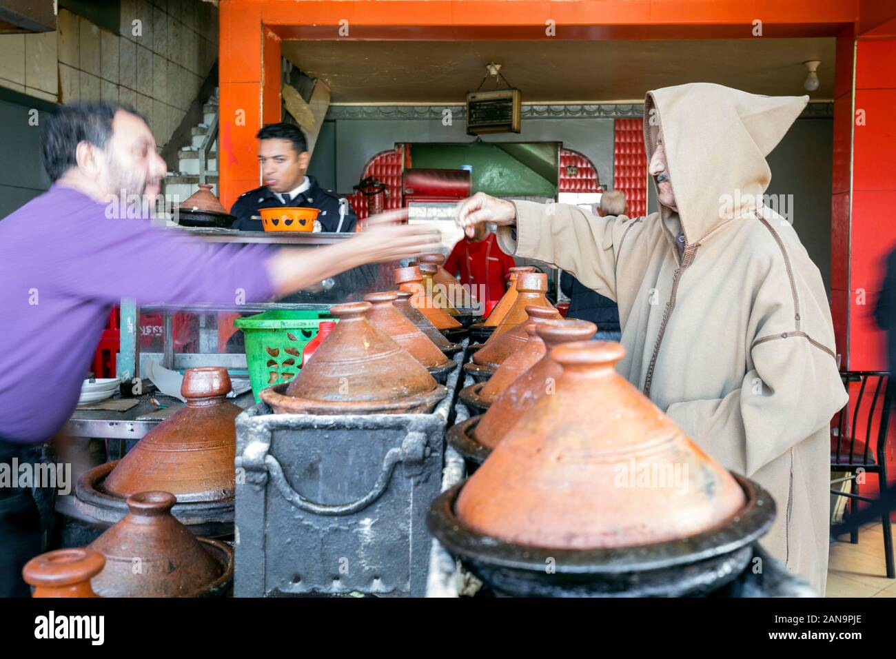 Marrakech, Maroc - Janvier 7,2020 : homme berbère traditionnel en tissu avec l'achat hotte tajine délicieux préparés et servis dans des contenants d'argile Banque D'Images