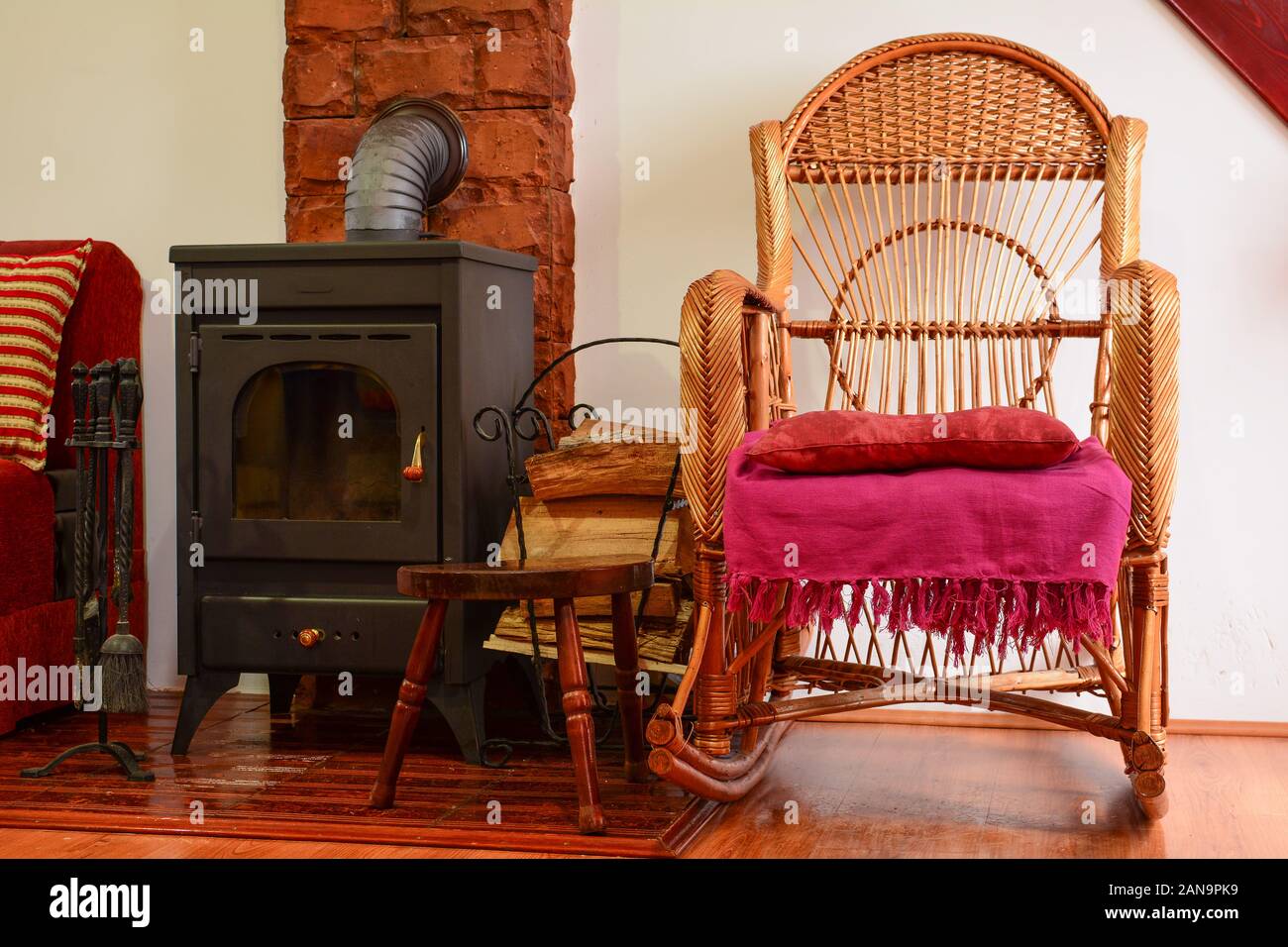 Coin repos avec wicker chair en plus d'un poêle à bois, petit tas de bois de chauffage et certains accessoires cuisinière Banque D'Images