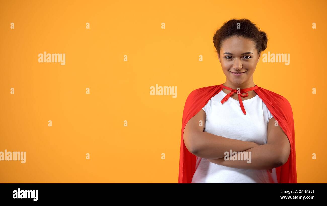 Jeune femme confiante en cape rouge sur fond lumineux, puissant wonder woman Banque D'Images