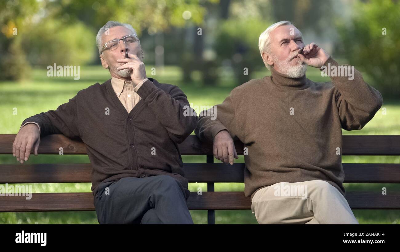 Les retraités hommes fumeurs de cigares coûteux, de repos dans le parc, bonne retraite Banque D'Images