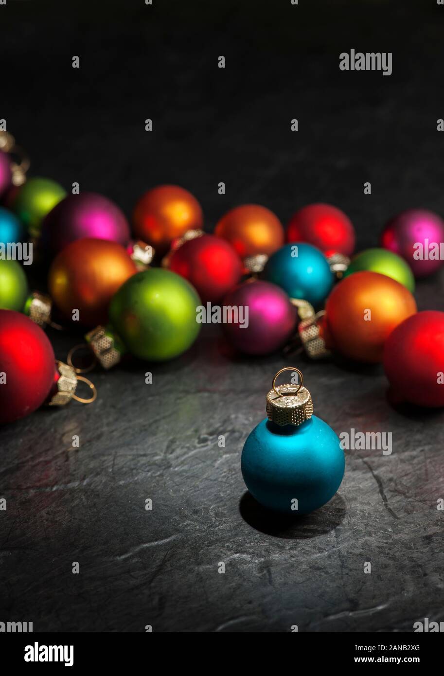 Les petites boules de Noël floue colorée sur une plaque en ardoise avec une seule boule de noël bleu permanent dans la forte avant-plan. Banque D'Images