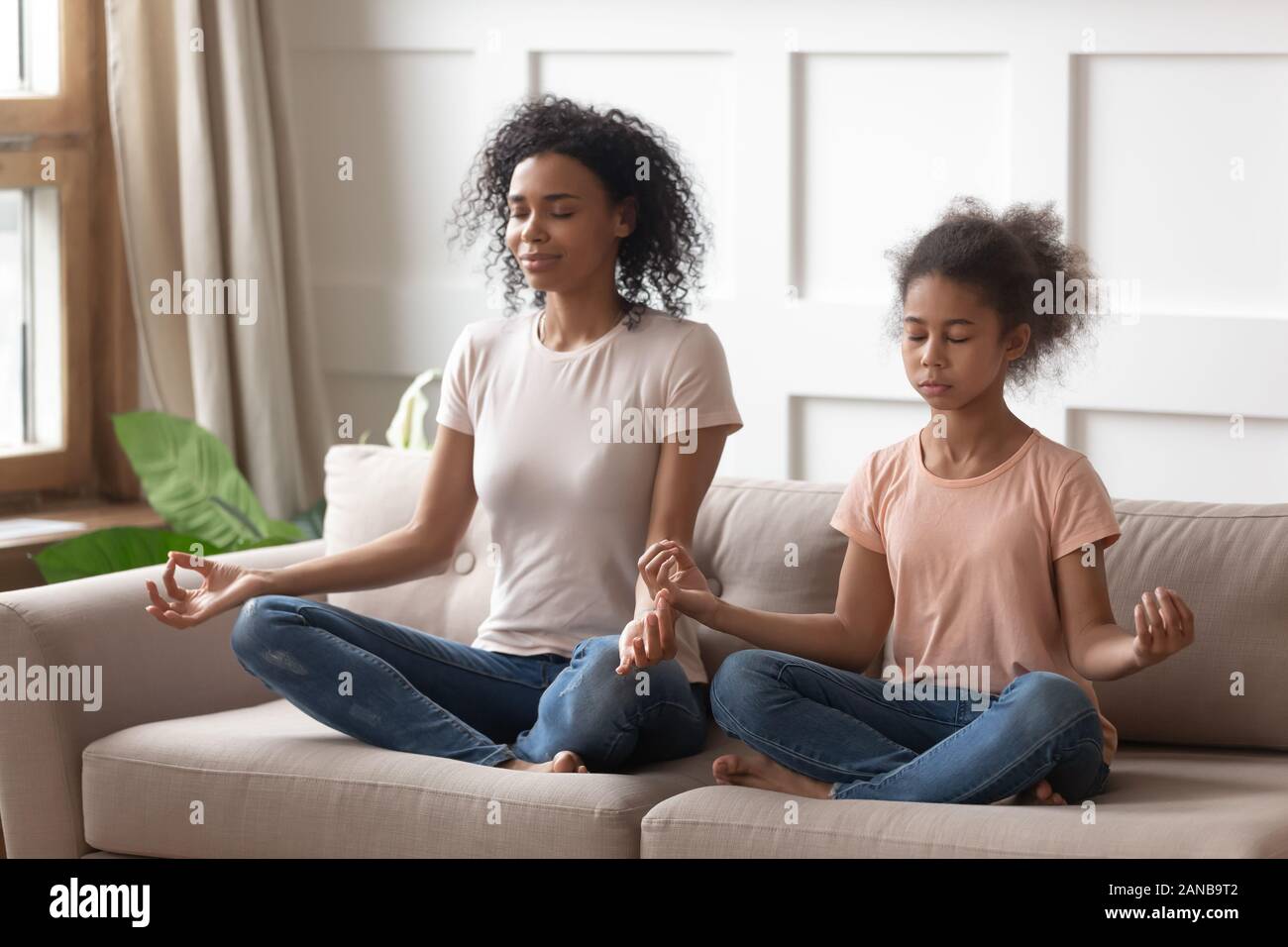 Mère et fille noire faisant les exercices de yoga à la maison. Banque D'Images