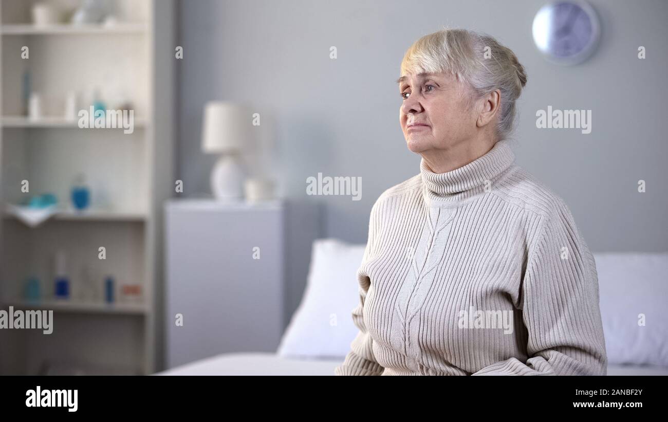 Contrarié femme âgée assise seule dans la maison de soins infirmiers, abandonnés par des parents Banque D'Images