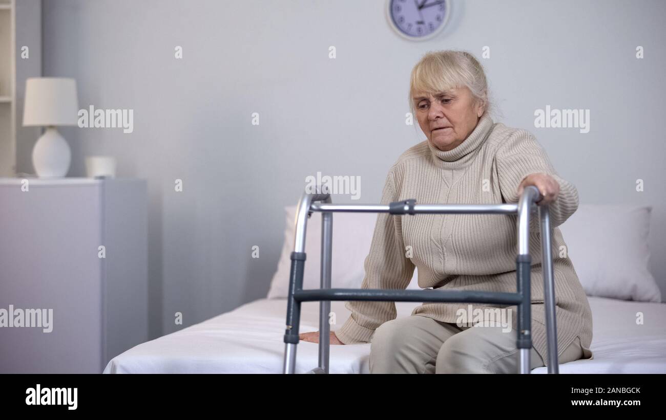 Grand-mère lit assis près de déambulateur, difficultés de réadaptation, santé Banque D'Images