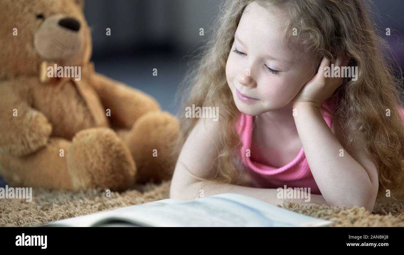 Concentrés cute girl reading book, allongé sur le tapis, l'éducation préscolaire Banque D'Images