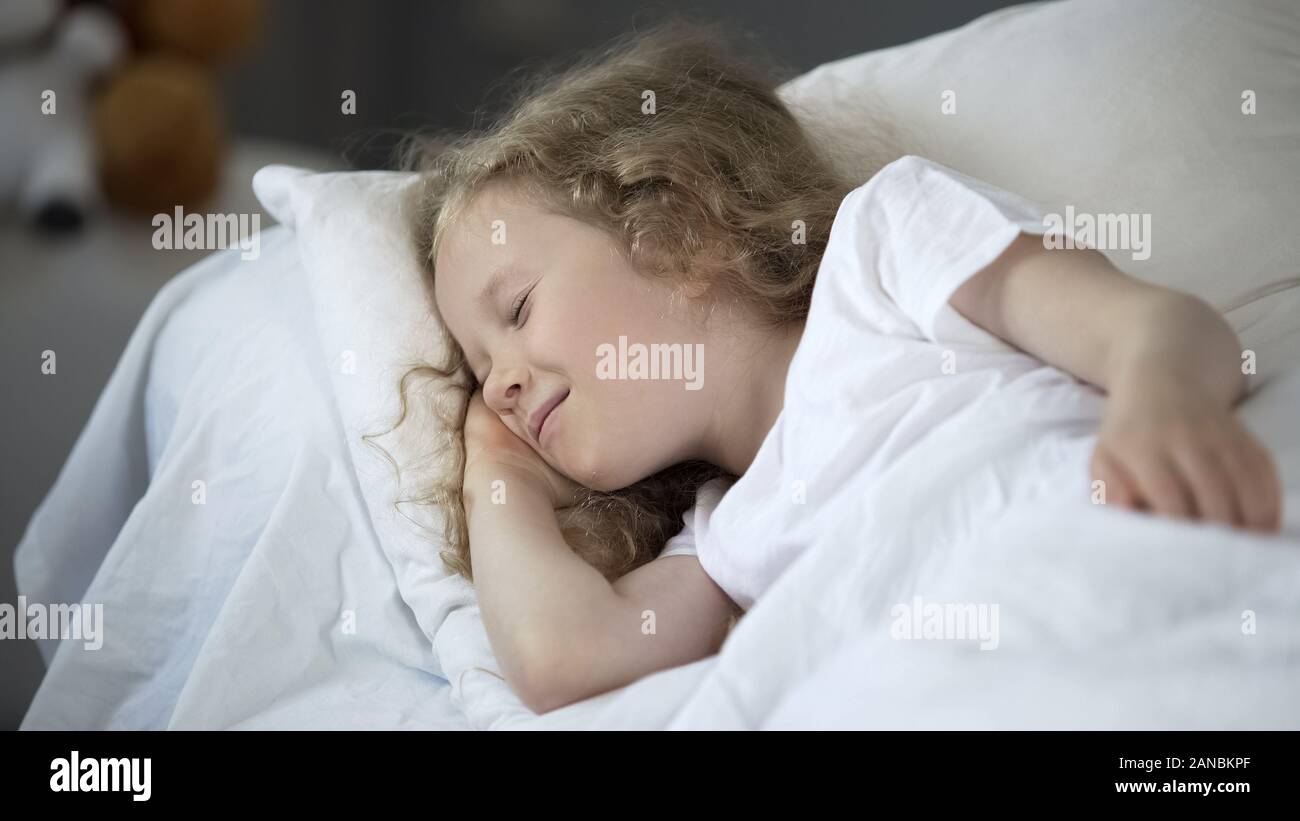 Happy young girl enjoying good dreams dans lit chaud, souriant alors que l'enfant endormi Banque D'Images