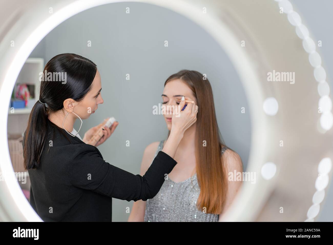 Maquilleuse faisant du maquillage à la femme aux yeux bleus par pinceau et ombre à paupières Banque D'Images