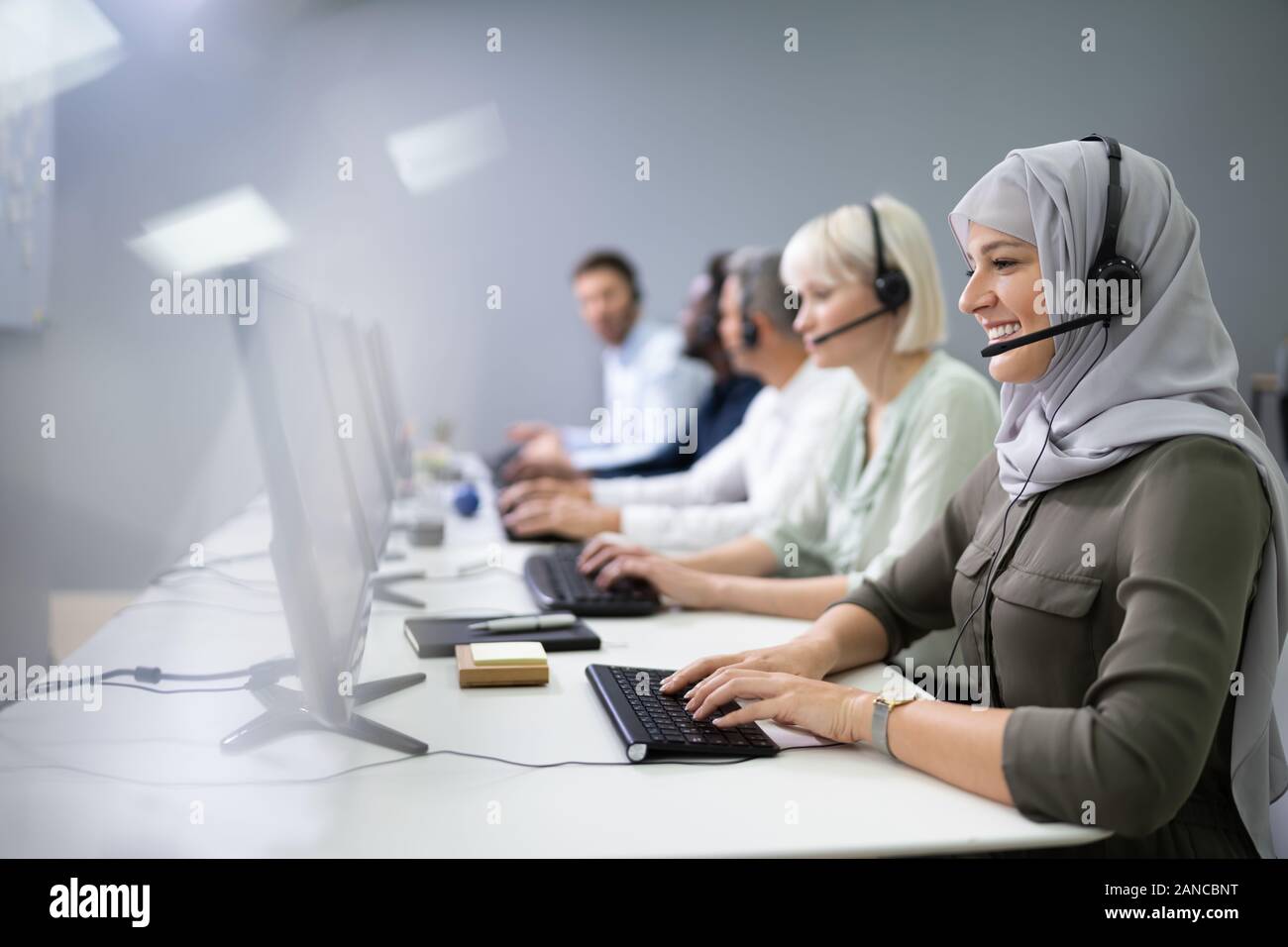 L'agent des services à la clientèle féminine positive avec casque de travail dans un centre d'appels Banque D'Images