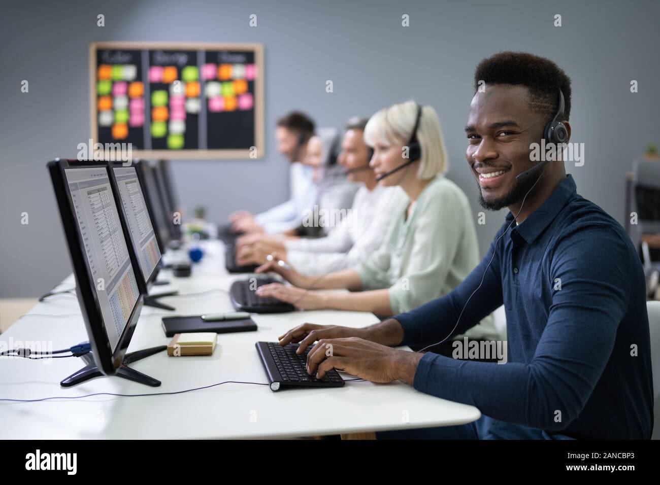 L'agent des services à la clientèle masculine positive avec casque de travail dans un centre d'appels Banque D'Images