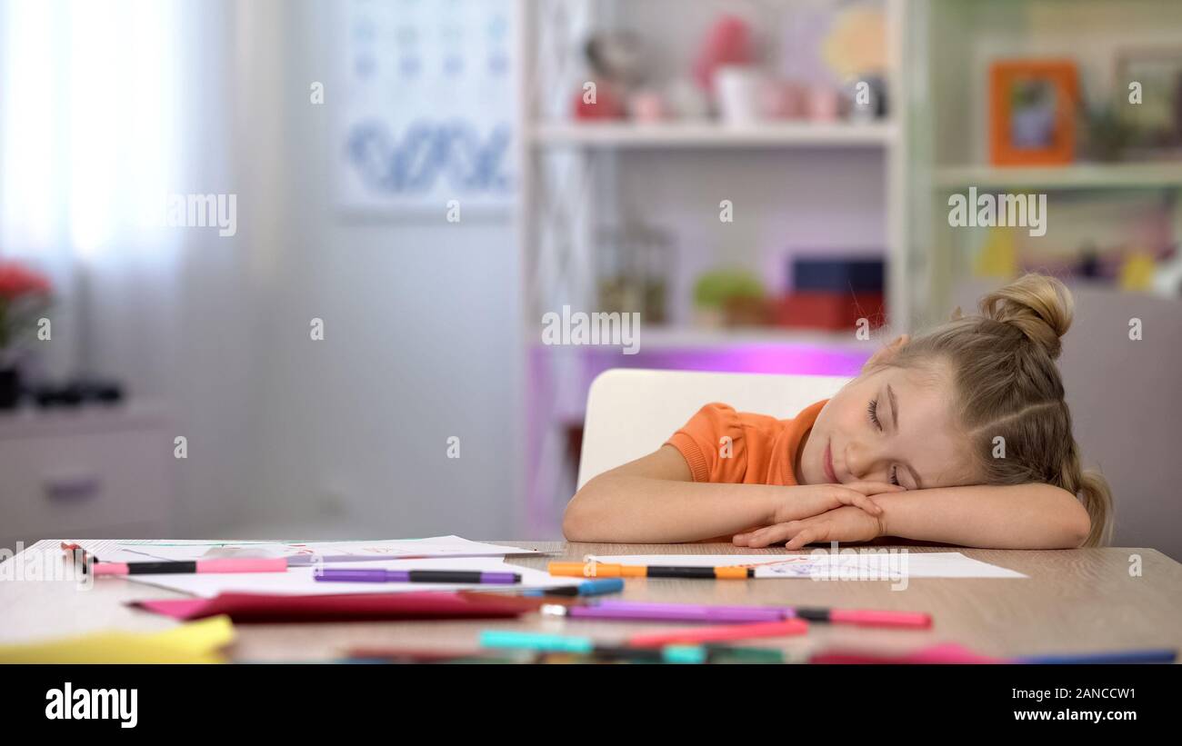 Adorable lycéenne dormir sur bureau, crayons de couleur et sur l'éducation tableau Banque D'Images