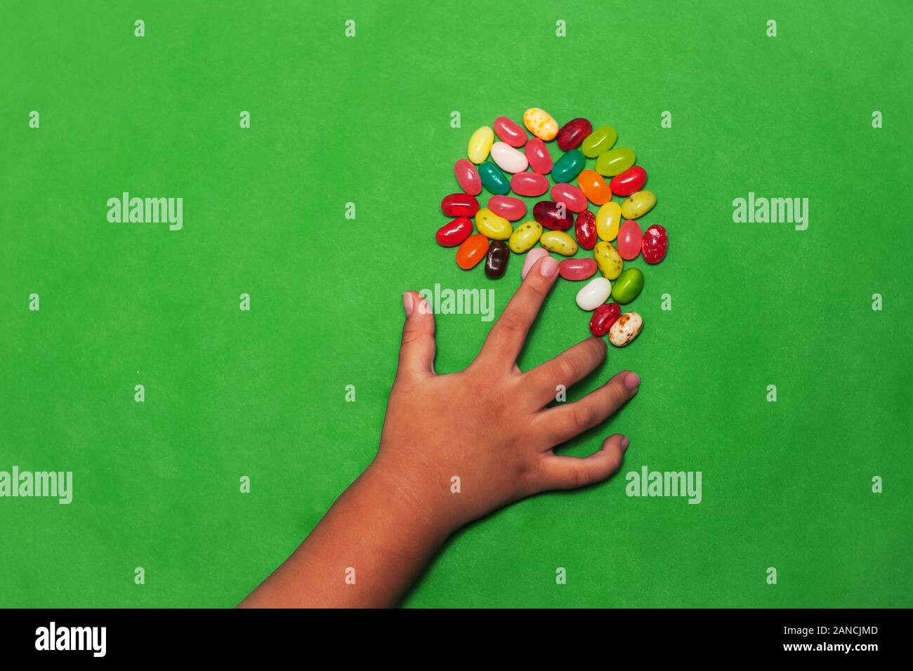 Un peu de mini hand reaching for un tas de bonbons en forme de différentes saveurs, avec un solide fond vert. Banque D'Images