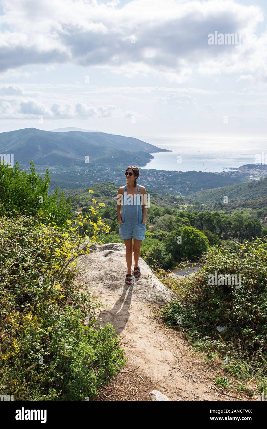 Young woman admiring panorama à partir de la colline qui surplombe le port de baie en Toscane denim dungaree Banque D'Images
