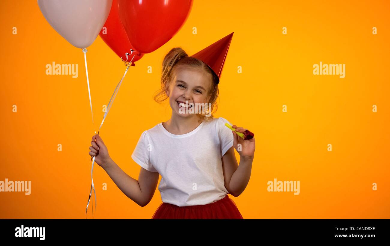 Fille mignonne avec ballons et soufflante parti souriant pour appareil photo, célébration Banque D'Images