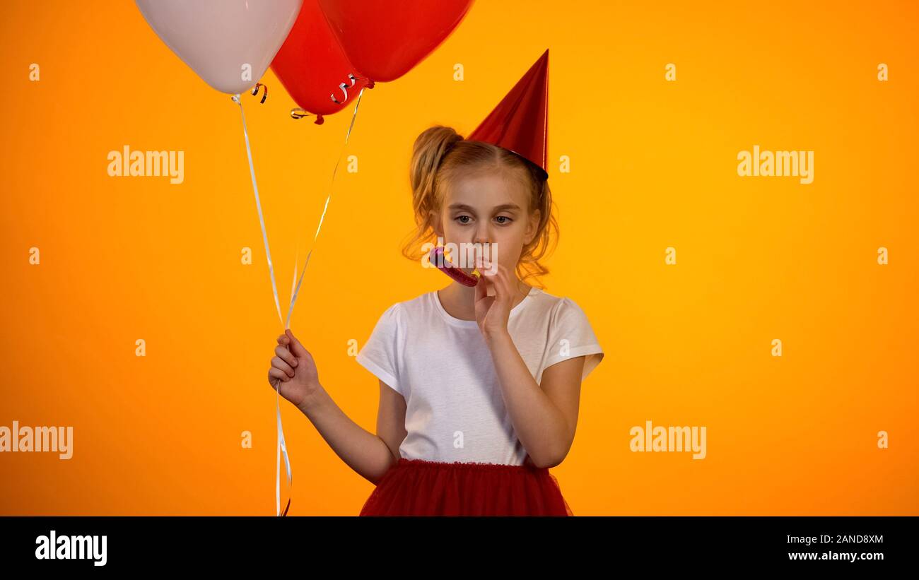 Malheureux Seul girl blowing party horn et holding balloons celebrating birthday Banque D'Images