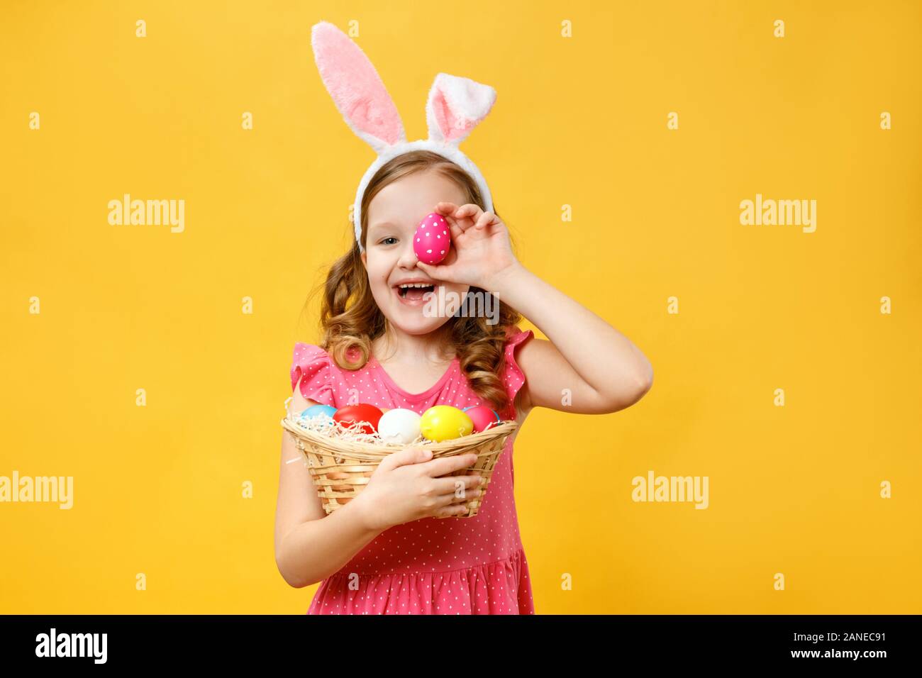 Heureux l'enfant dans les oreilles d'un lapin est titulaire d'un oeuf de Pâques et un panier. Portrait d'une petite fille sur un fond jaune. Banque D'Images