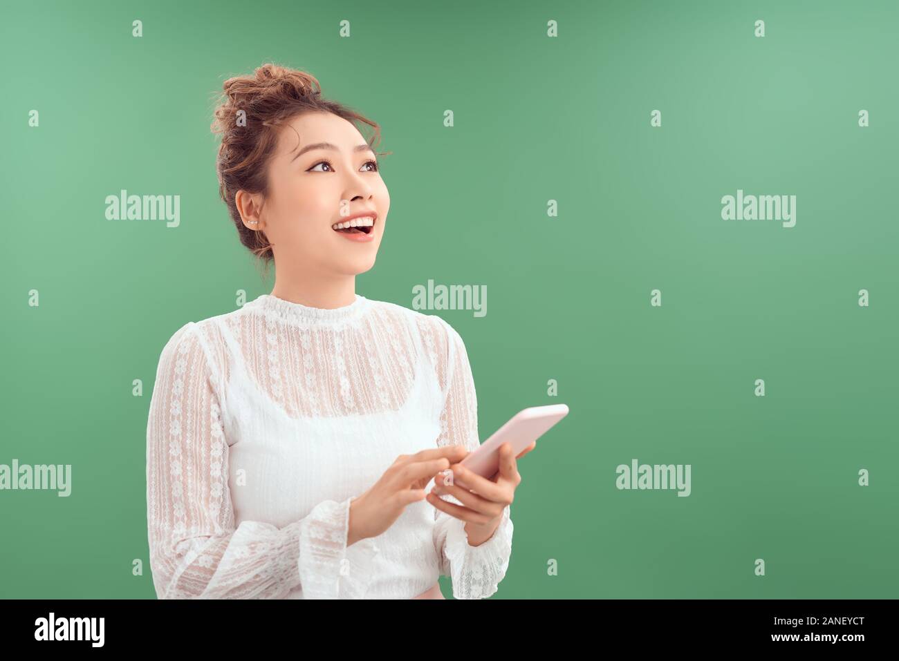 Happy Young Asian woman using mobile phone tout en regardant vers le haut. Isolé sur fond vert. Banque D'Images