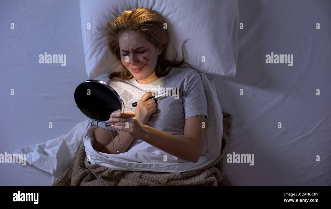 Dame pleurer avec plaie sur le visage à la recherche dans le miroir au lit,  la violence domestique Photo Stock - Alamy