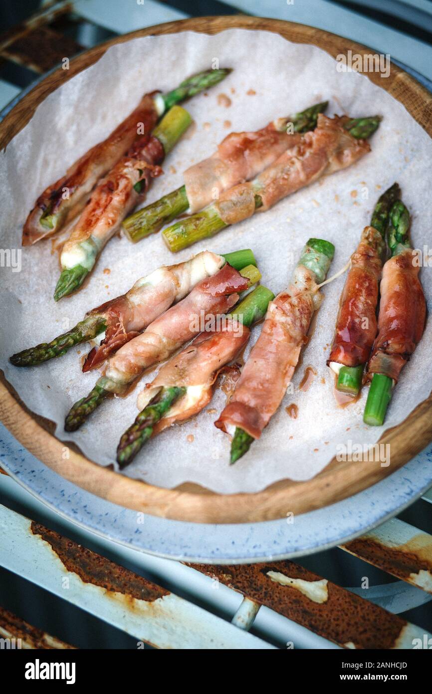 Buffet de plats - jambon de Parme et asperges enrobées de mozzerella servies sur une assiette sur un banc de pique-nique rose. Pose plate Banque D'Images