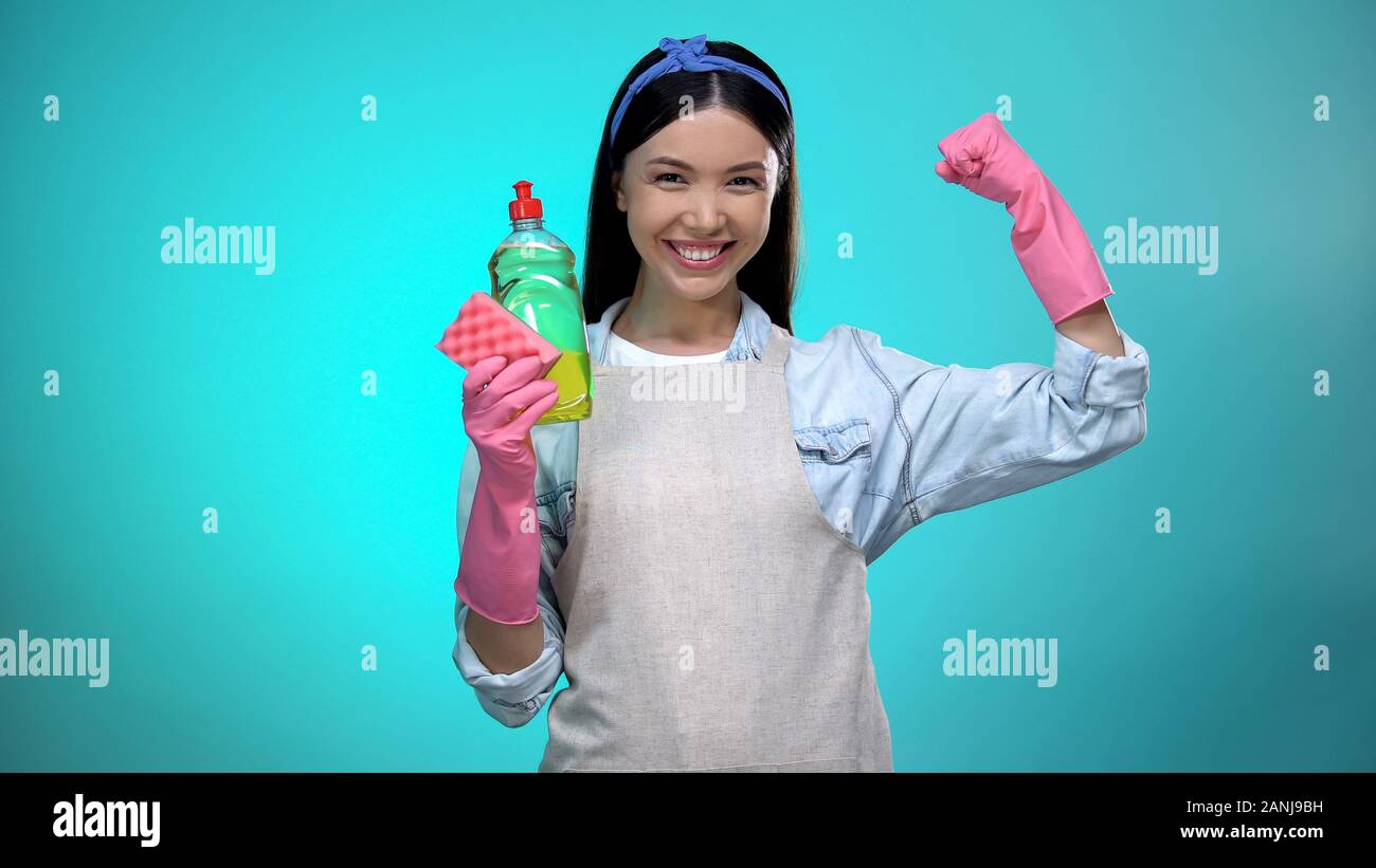 Femme au foyer avec un liquide vaisselle sourire montrant les muscles, signe de la force Banque D'Images